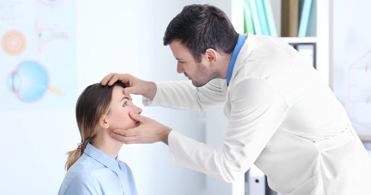 A medical professional examines a patient's face, likely checking for eye-related issues in a clinical setting.