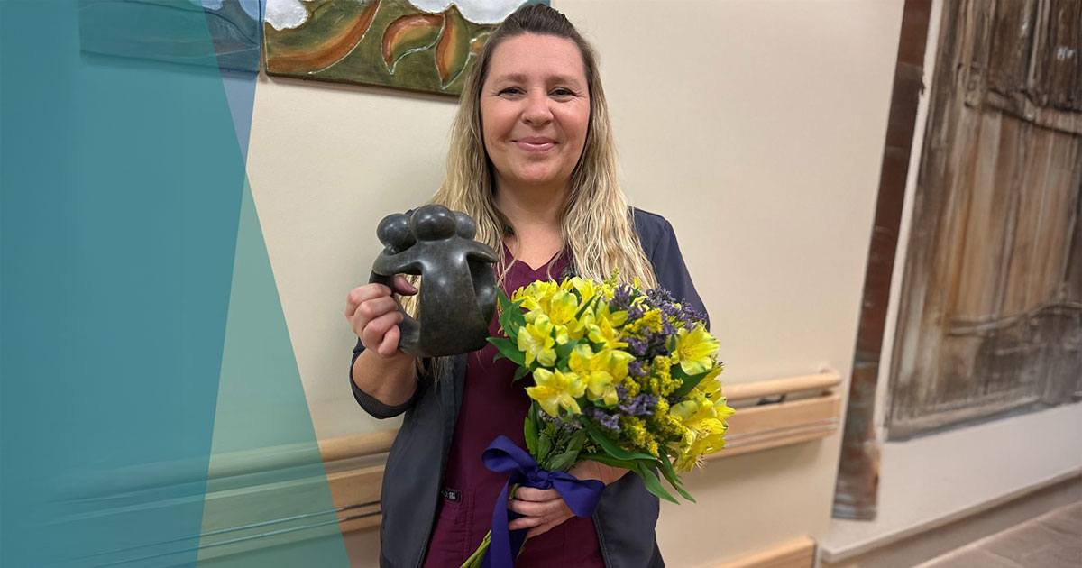 A woman holds a bouquet of flowers and a small sculpture, smiling against a wall with artwork.