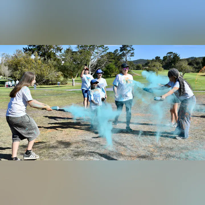 A group of people at an outdoor event spray colorful powder, celebrating and having fun.