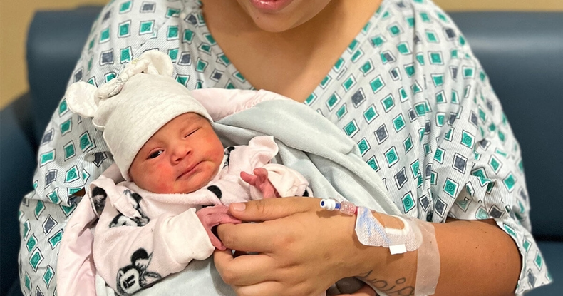 A new mother holds her baby in a hospital setting, both looking content and cozy, with the mother wearing a hospital gown.
