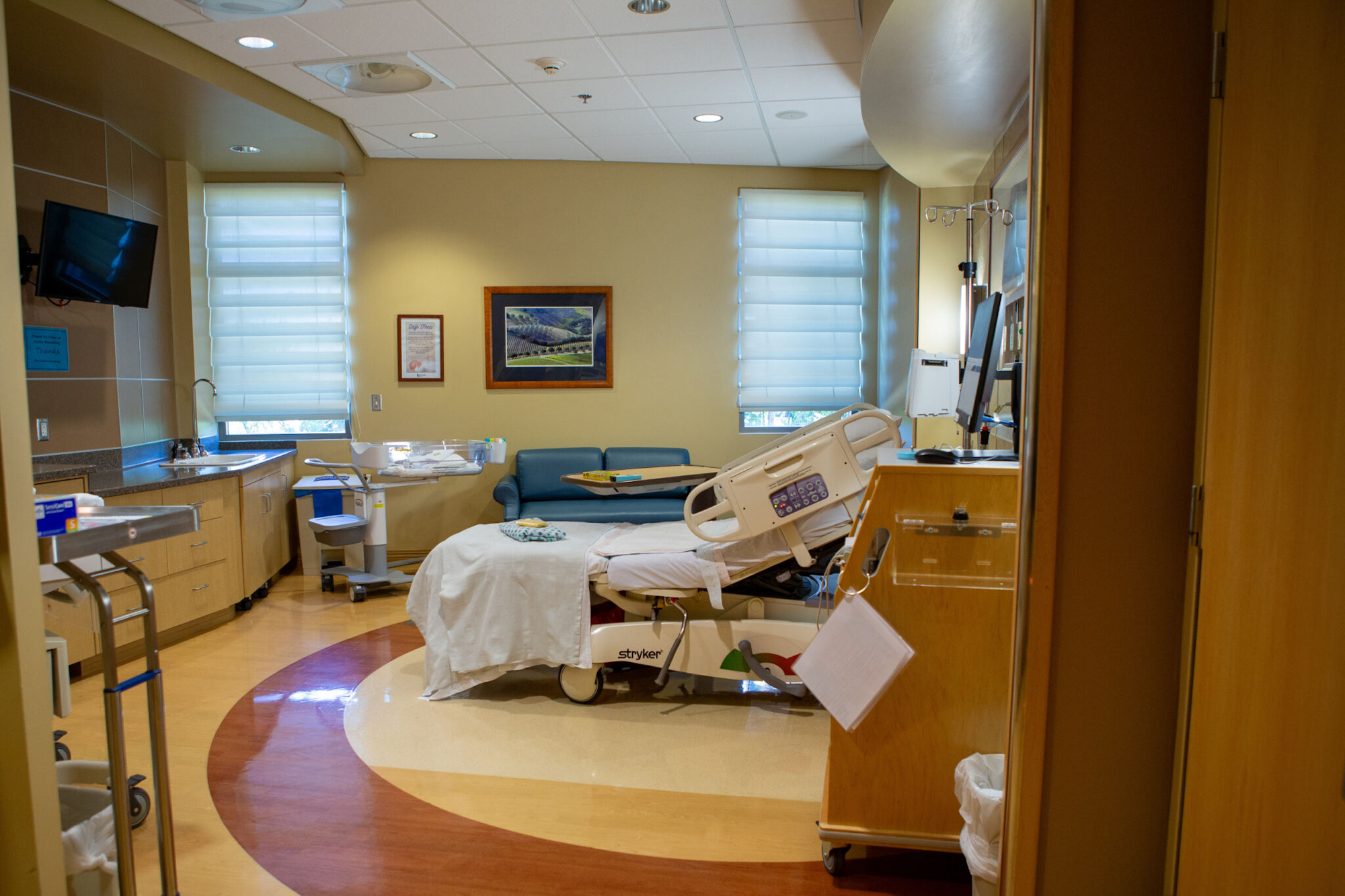 The image shows a hospital room with a bed, medical equipment, a sofa, and natural light from the window.