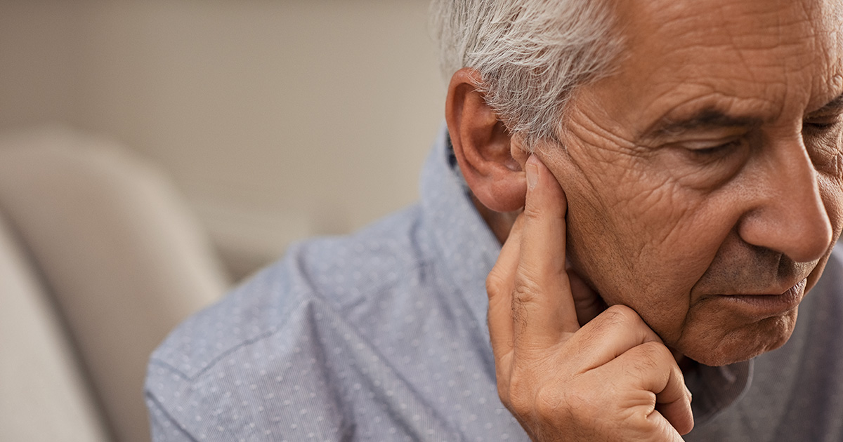 An older man looks pensive, touching his ear, possibly indicating a concern or discomfort.