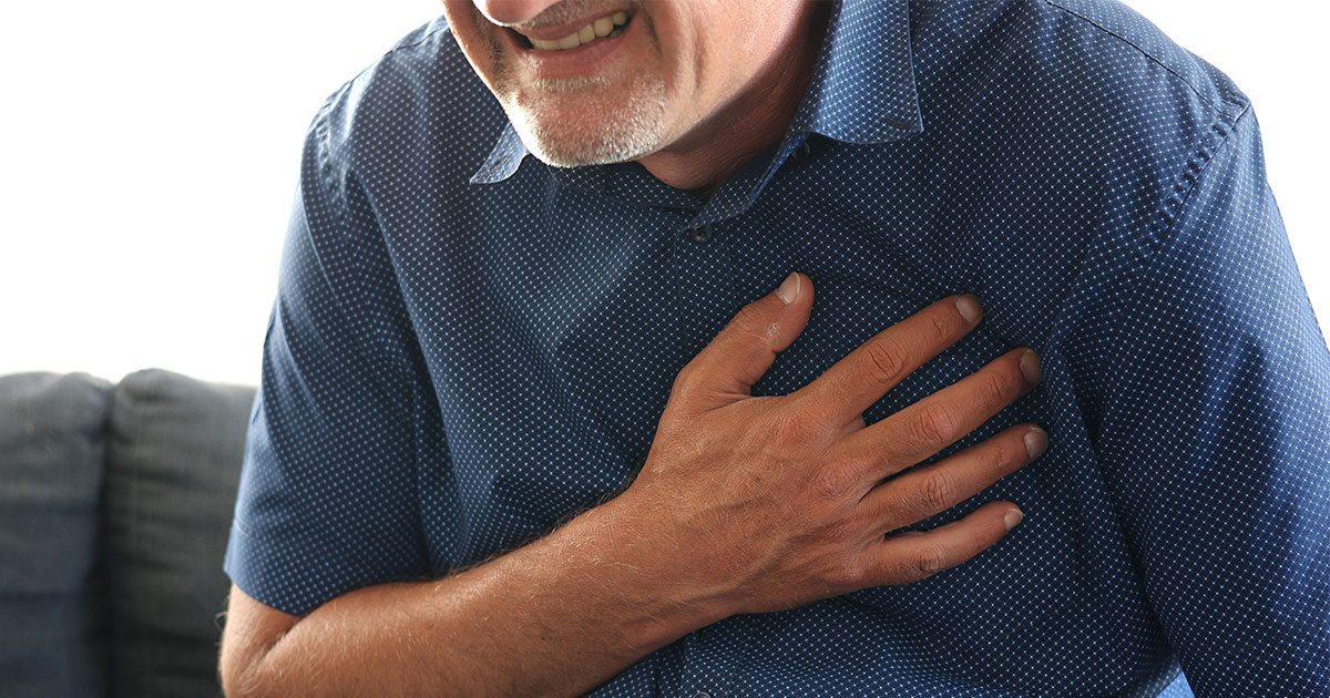 A man clutches his chest, possibly experiencing discomfort or pain. The setting appears to be indoors.