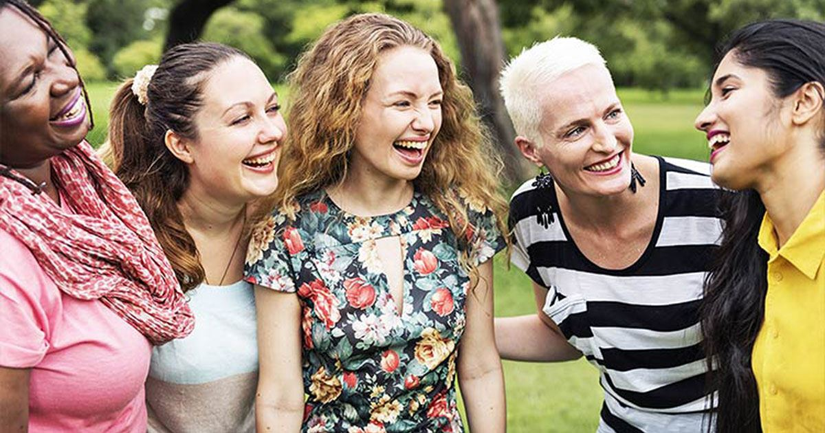 A group of five women laughing and enjoying each other's company outdoors, showcasing smiles and friendship.