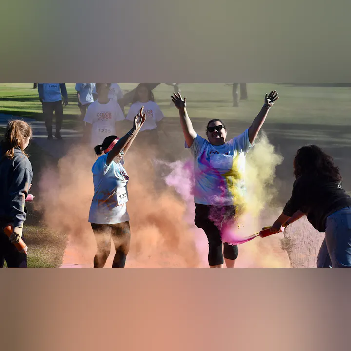 Participants celebrate in a colorful, vibrant event, covered in bright powder amid cheers and excitement.
