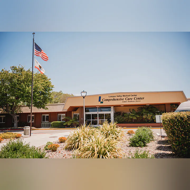 The image shows the Lompoc Valley Medical Center's Comprehensive Care Center with flags and landscaped surroundings.