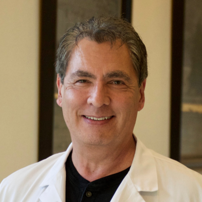 A smiling person wearing a white lab coat, posing in a professional setting.