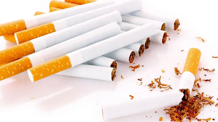 The image shows a collection of cigarettes, some whole and one broken with tobacco spilling out.