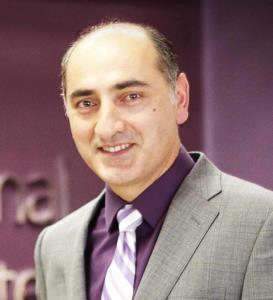 The image shows a man in a suit and tie, smiling against a backdrop with text.