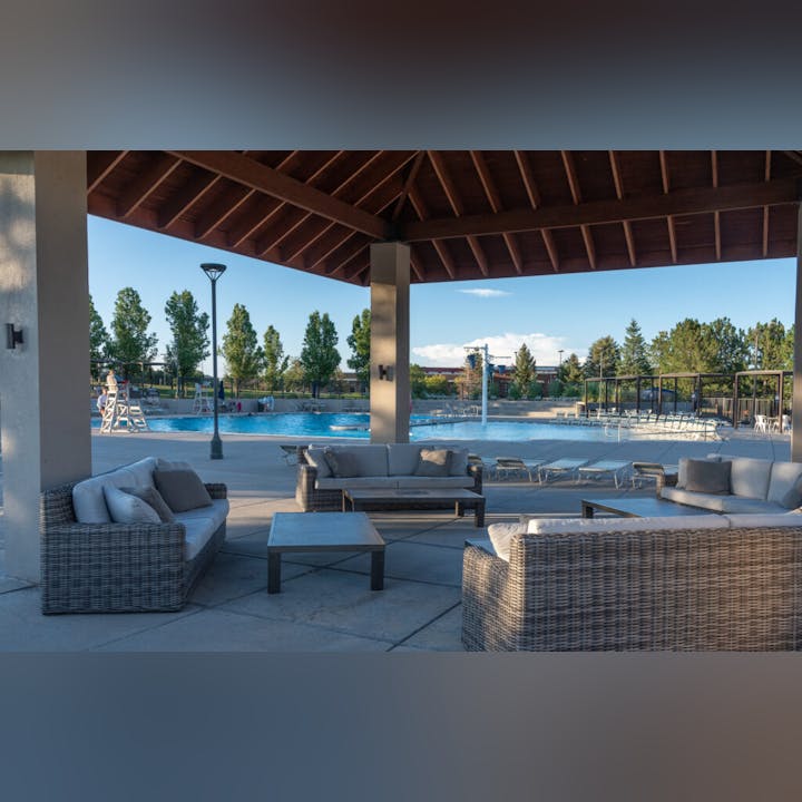 Outdoor pool area with lounging furniture and trees under a clear sky.