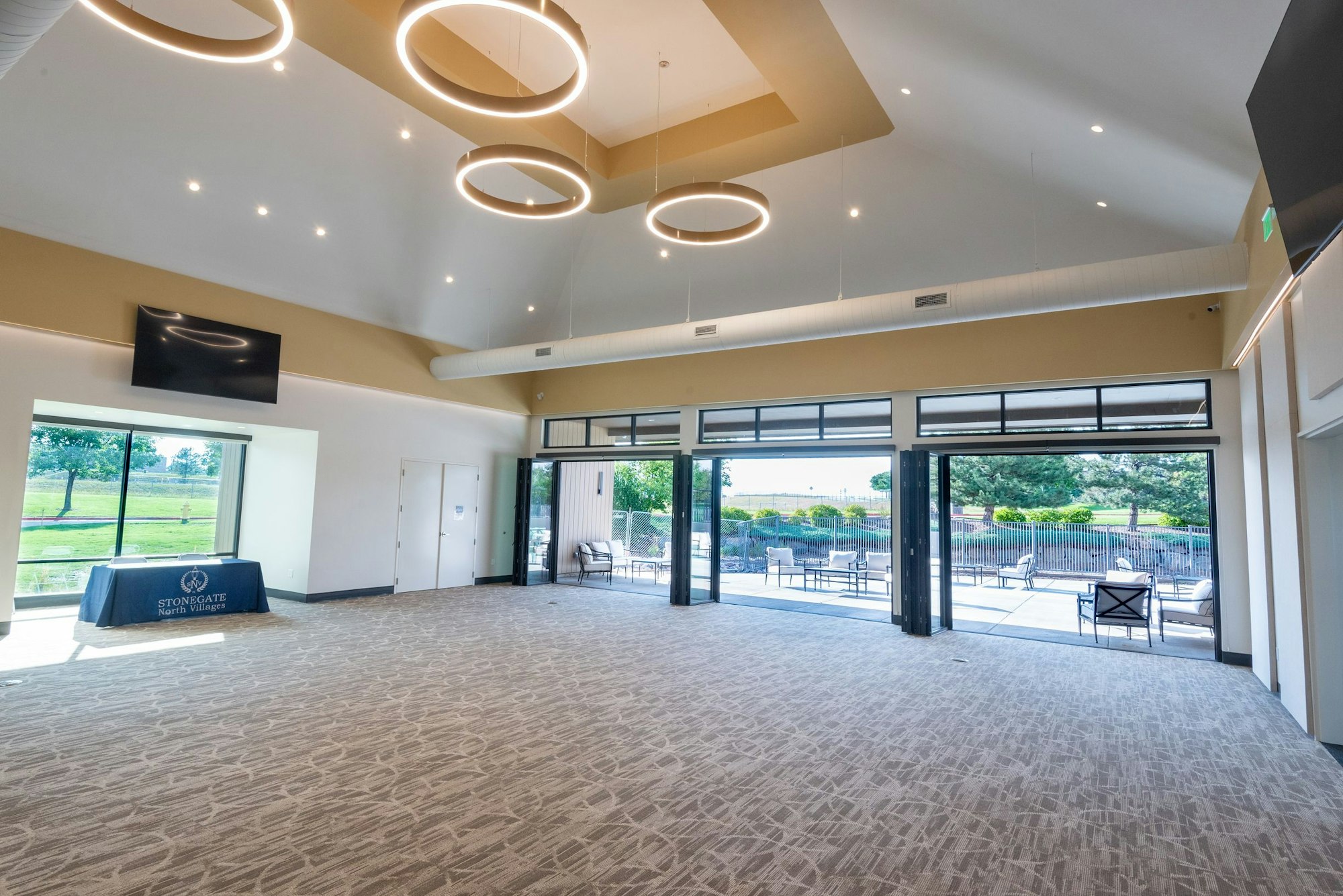 Modern event hall with ring-shaped lights, carpet flooring, and glass doors leading to outdoor seating area.