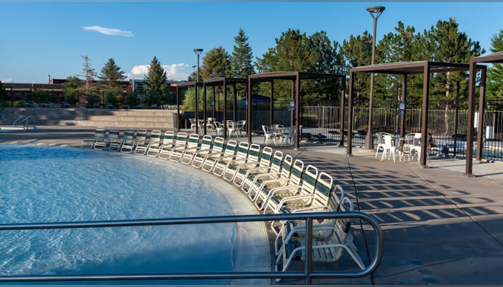 Outdoor swimming pool with loungers and shaded tables, on a sunny day.