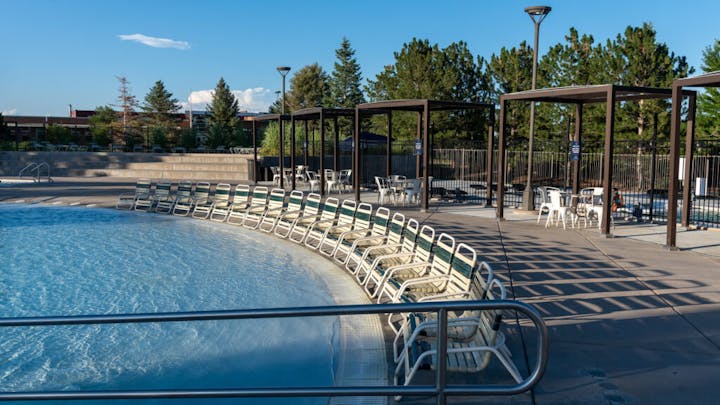 Outdoor swimming pool with loungers and shaded tables, on a sunny day.