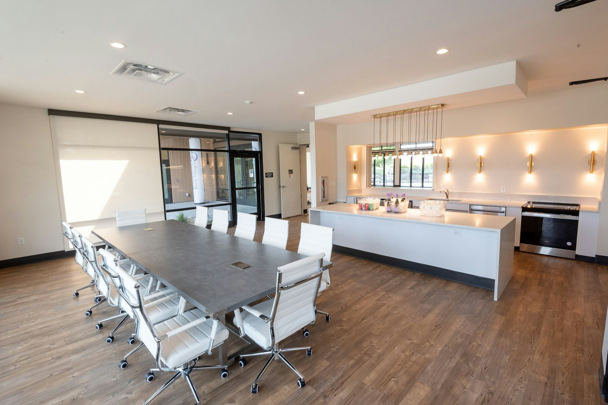 Modern meeting room with a large table, chairs, kitchenette, and ample lighting.