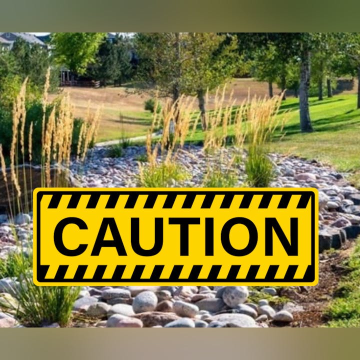 A natural landscape with grass and stones, featuring a large yellow "CAUTION" sign in the foreground.