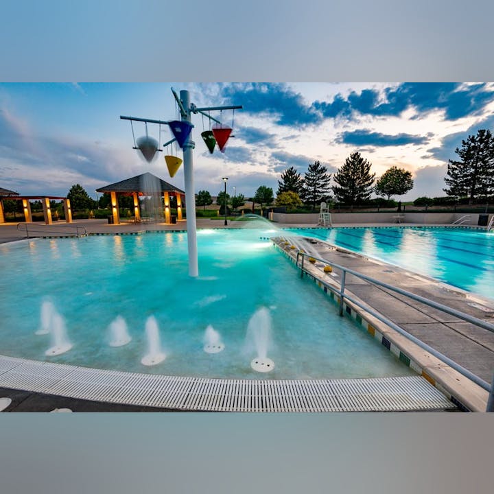 A colorful public swimming pool with fountains, buckets, and sunset sky.