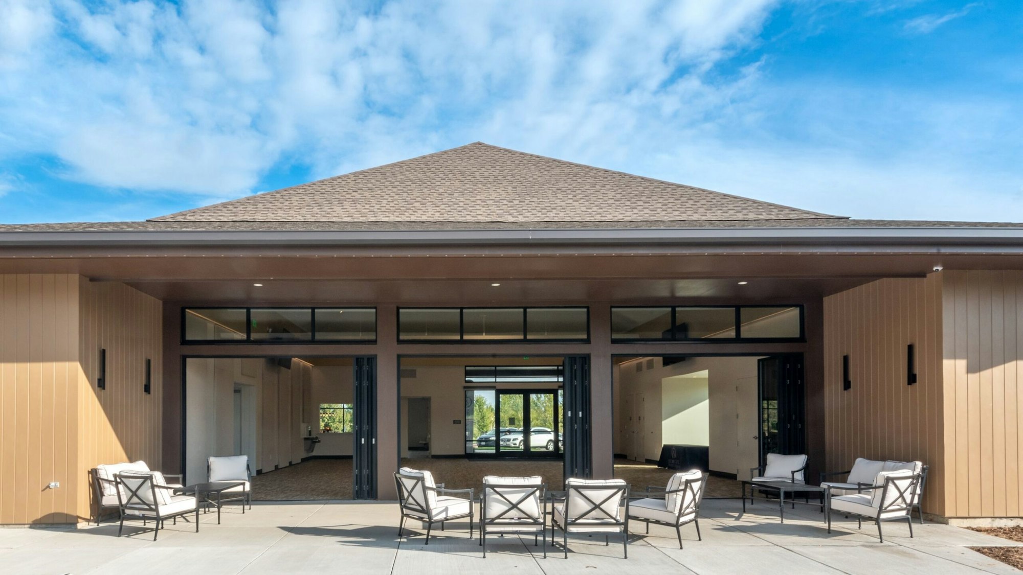 Modern building with large windows, patio seating, under a clear blue sky.