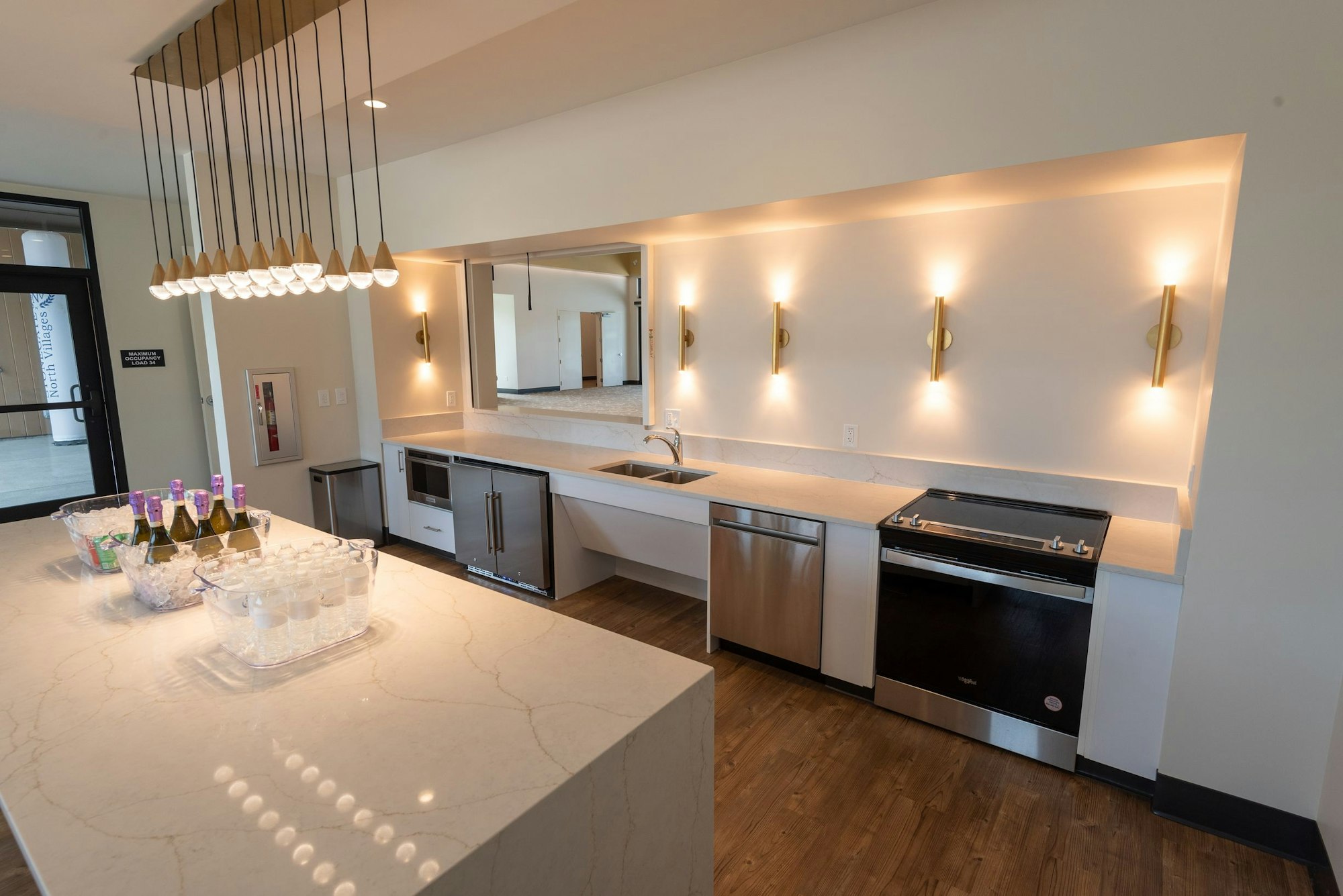 Modern kitchen with island, pendant lights, wine bottles, and glasses set for an event.