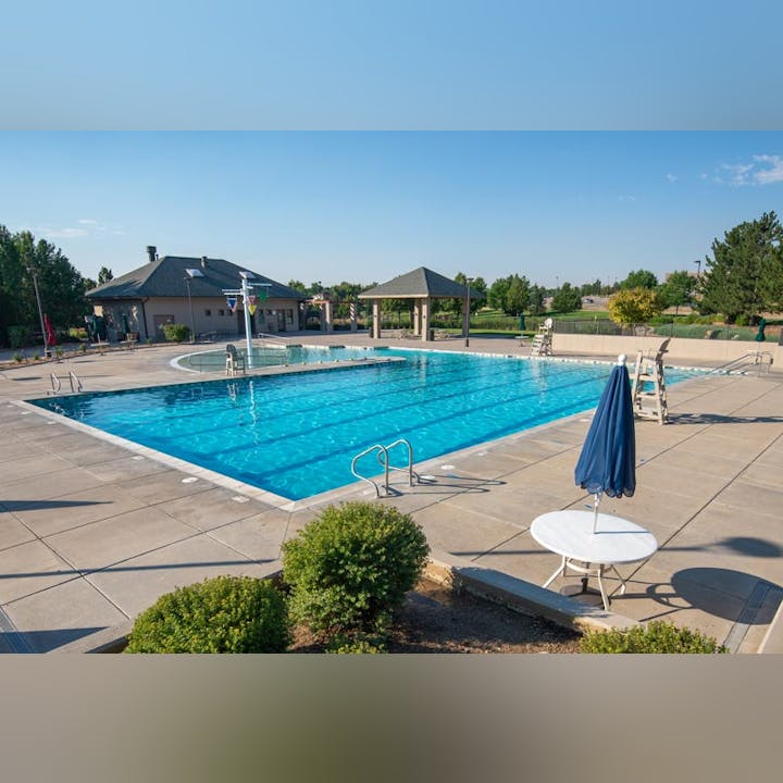 A serene outdoor swimming pool area with buildings, lounging chairs, and a closed umbrella on a sunny day.