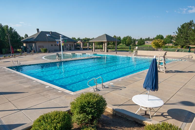A serene outdoor swimming pool area with buildings, lounging chairs, and a closed umbrella on a sunny day.