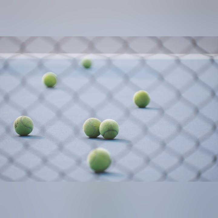 Tennis balls scattered on a court, viewed through a chain-link fence.