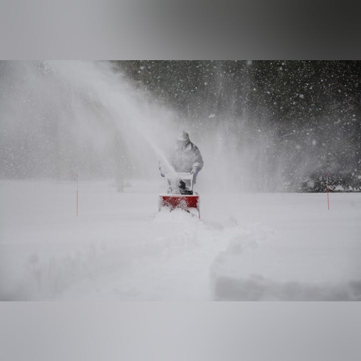 A person using a snowblower amidst heavy snowfall.