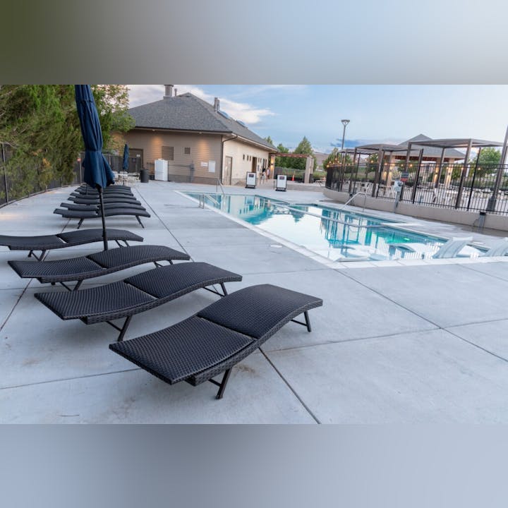 Outdoor swimming pool with lounge chairs and closed umbrellas on a sunny day.