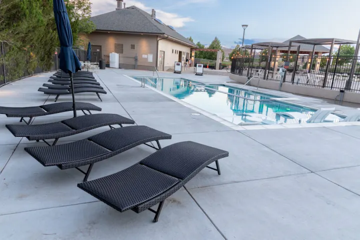 Outdoor swimming pool with lounge chairs and closed umbrellas on a sunny day.