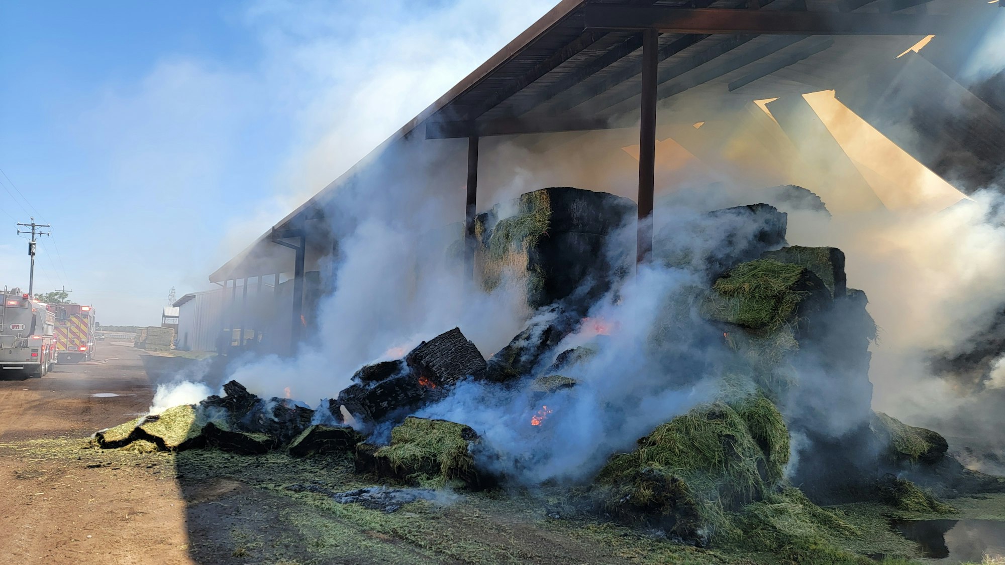 A barn with burning hay bales emitting smoke, with a fire truck nearby.