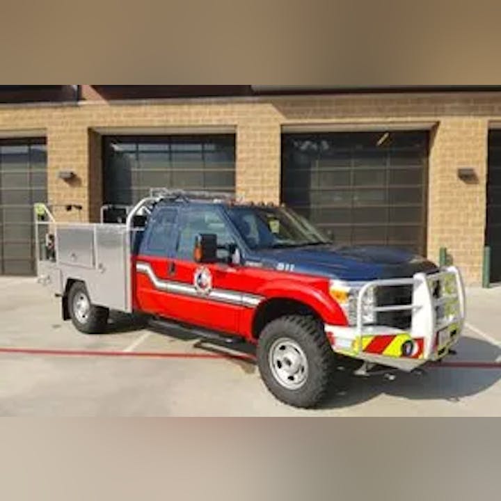 A red fire rescue truck with a specialized rear compartment, parked in front of a fire station.