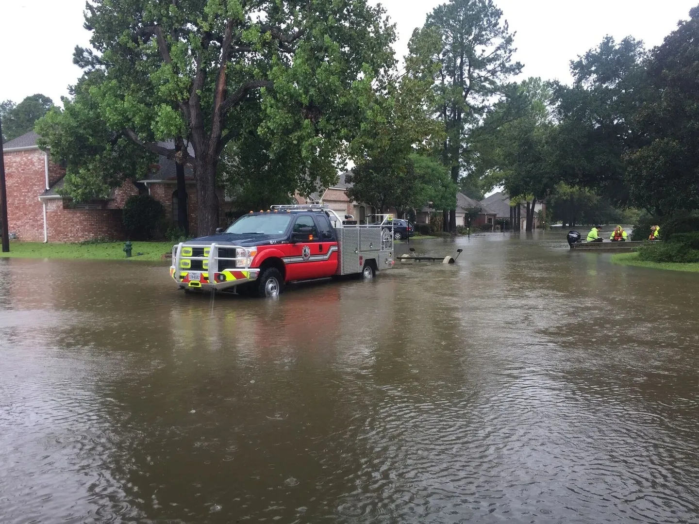 A fire truck and rescue boat in a flooded street with people in safety gear.