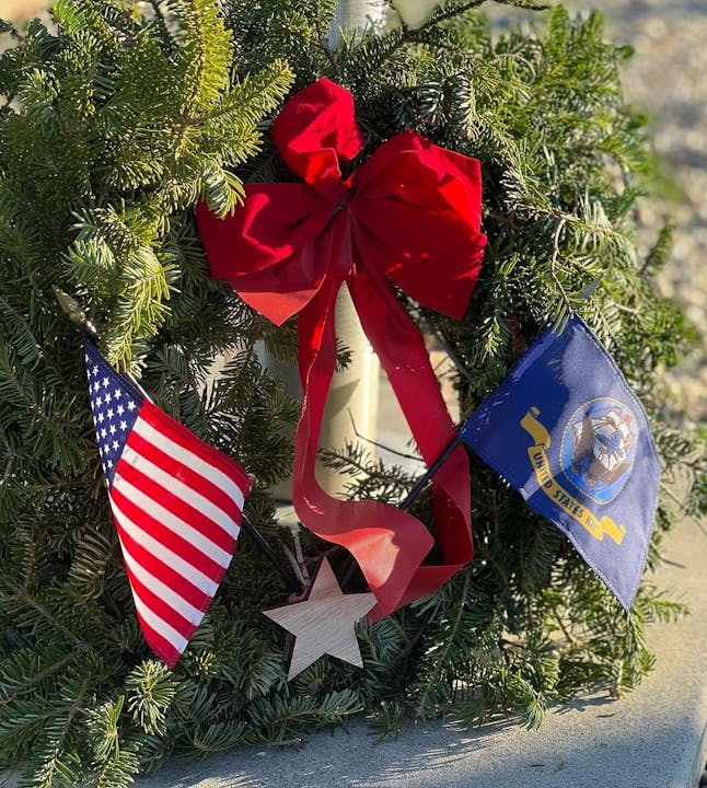 A festive wreath adorned with a red bow, a wooden star, and US and state flags.