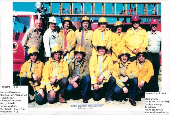 A group of firefighters in uniform in front of a fire truck. There's text indicating they belong to a volunteer fire department, dated February 1977.
