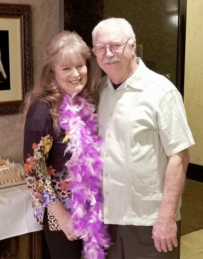 A smiling couple with the woman wearing a purple feather boa.