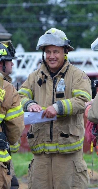 Firefighters in gear talking, one holding a paper.