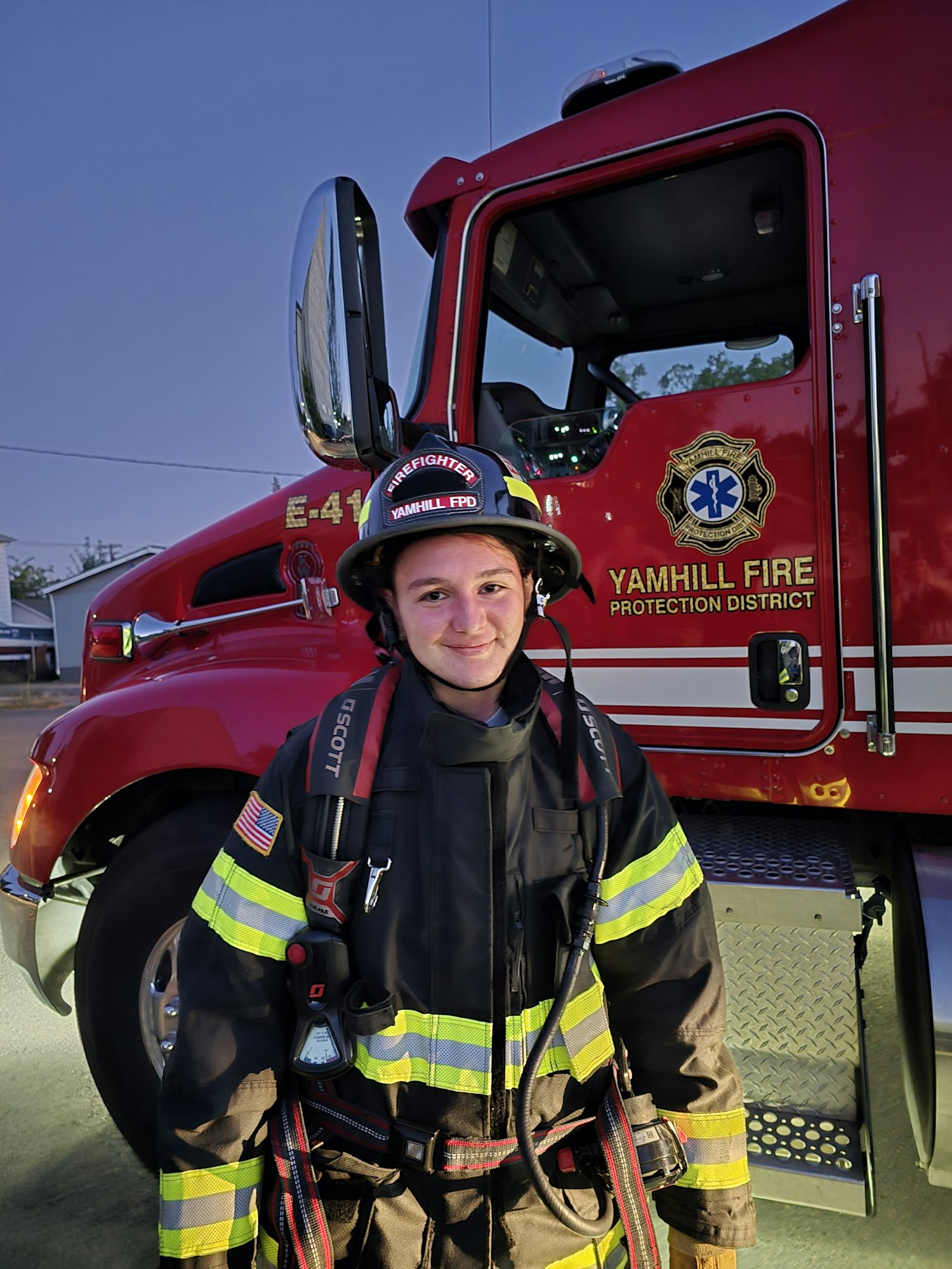 A firefighter in full gear is standing next to a red fire truck.