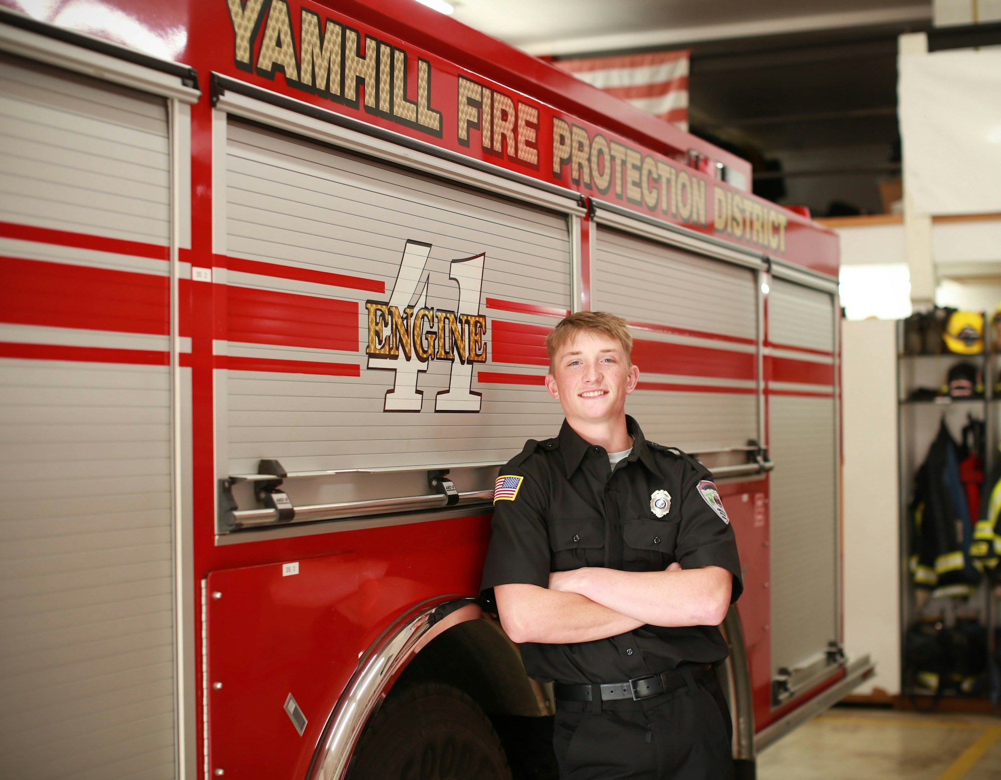 A firefighter in uniform smiling and leaning against a fire truck labeled "Yamhill Fire Protection District Engine 41."