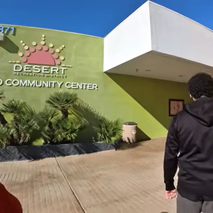 The image shows the Desert Recreation District Community Center with a sunny sky and a person walking towards it.