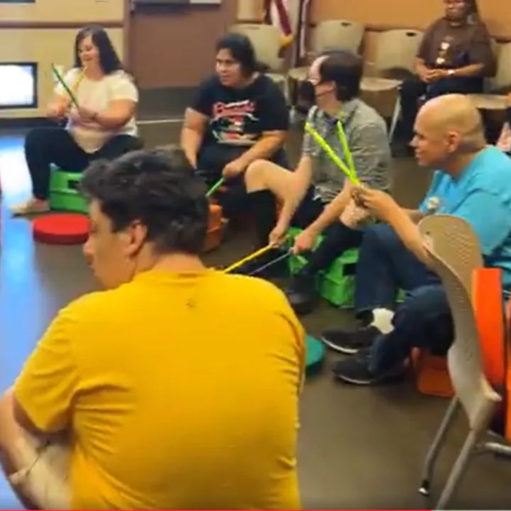 A group of people is sitting in a circle, playing rhythm instruments and engaging in a music activity together.