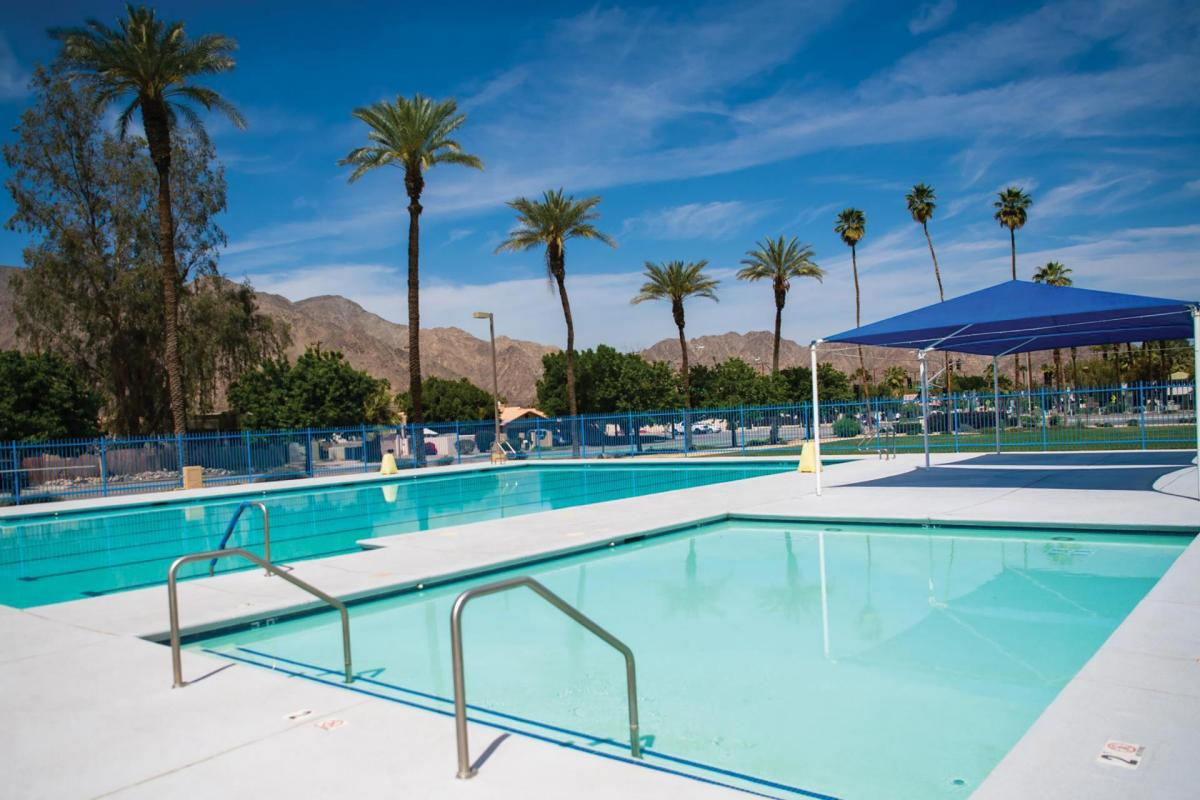 A tranquil pool area with palm trees, mountains in the background, and a blue sky, perfect for relaxation.