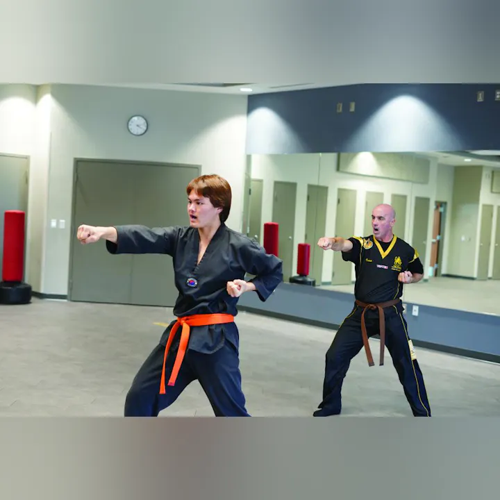 Two martial arts practitioners are sparring in a dojo, showcasing their skills and techniques in a training session.