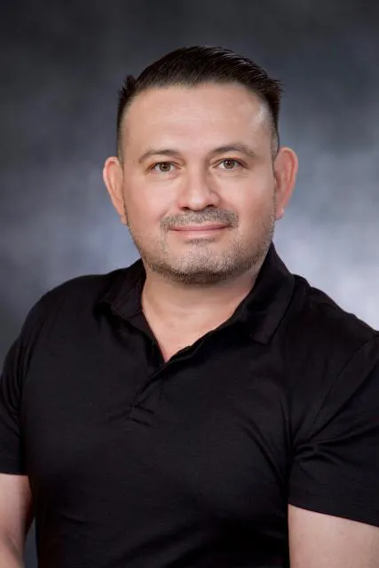 The image features a man with short hair wearing a black polo shirt, posing in front of a dark background.