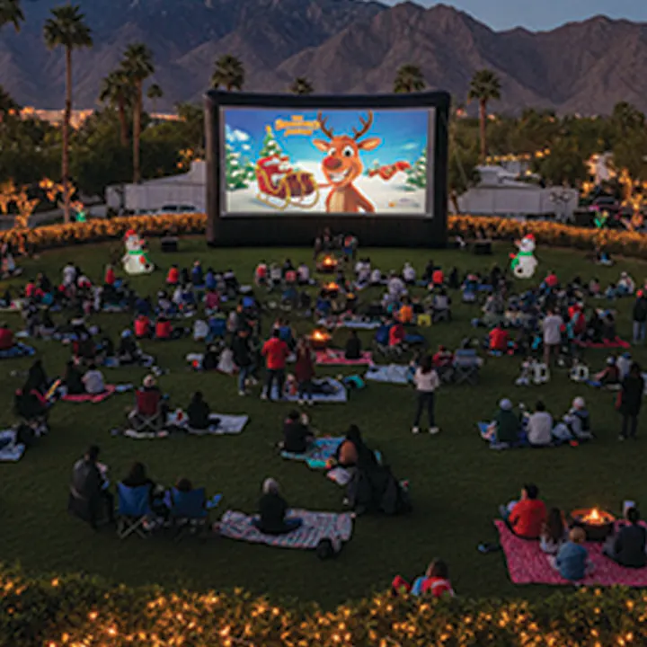 A crowd enjoying an outdoor movie screening with a festive theme, surrounded by decorations and mountains in the background.
