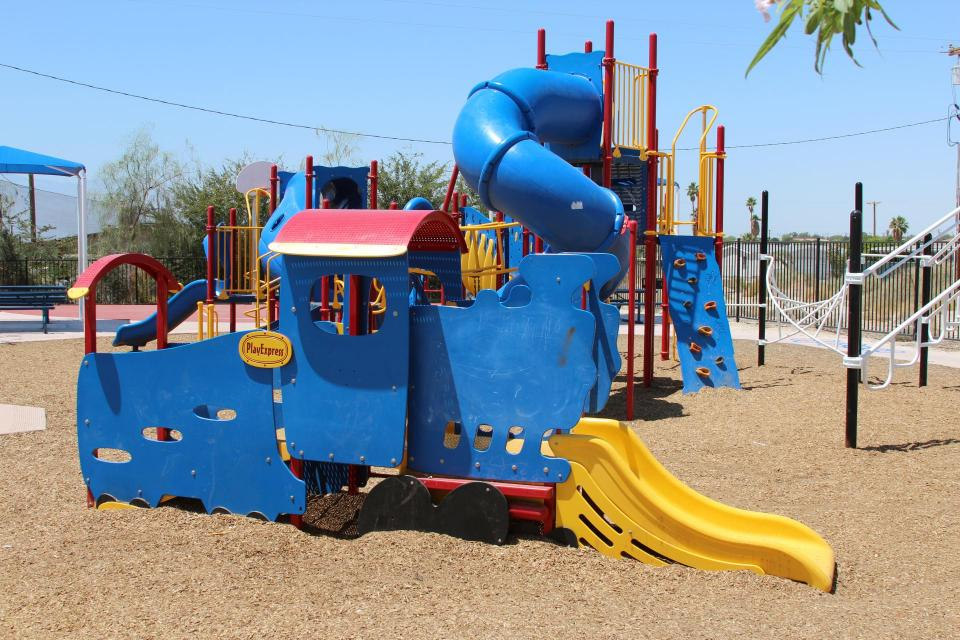 A colorful playground featuring a train-shaped structure with slides and climbing elements, set on a sandy surface.