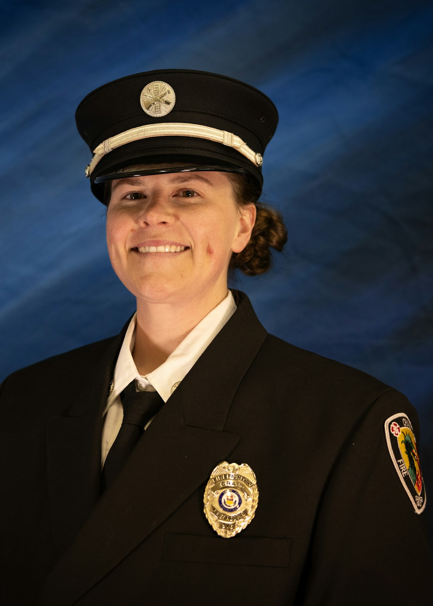 The image features a smiling female firefighter or emergency responder wearing a uniform and hat, posed against a blue background.