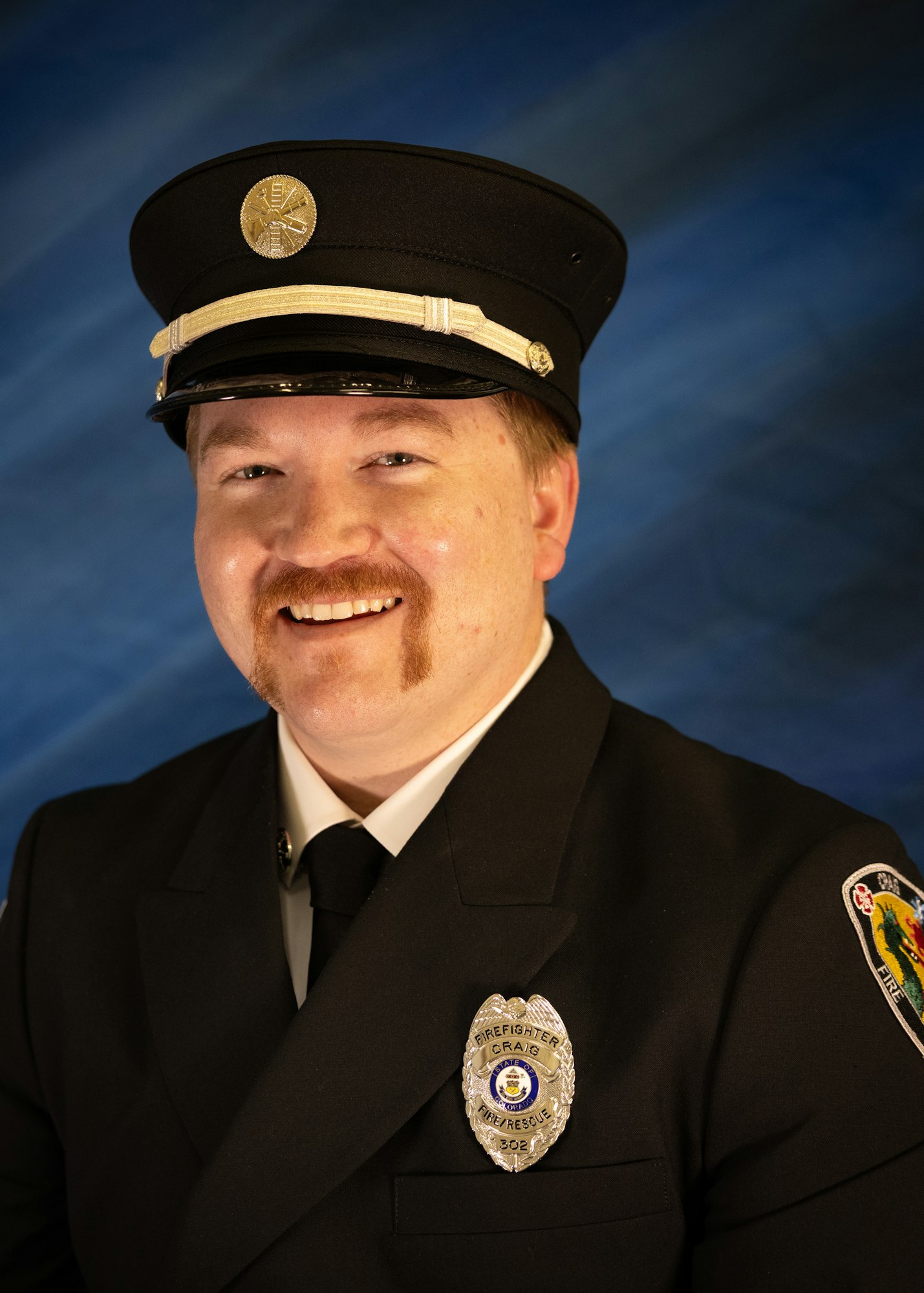 The image features a smiling individual in a firefighter's uniform and hat, with a badge visible on their chest.