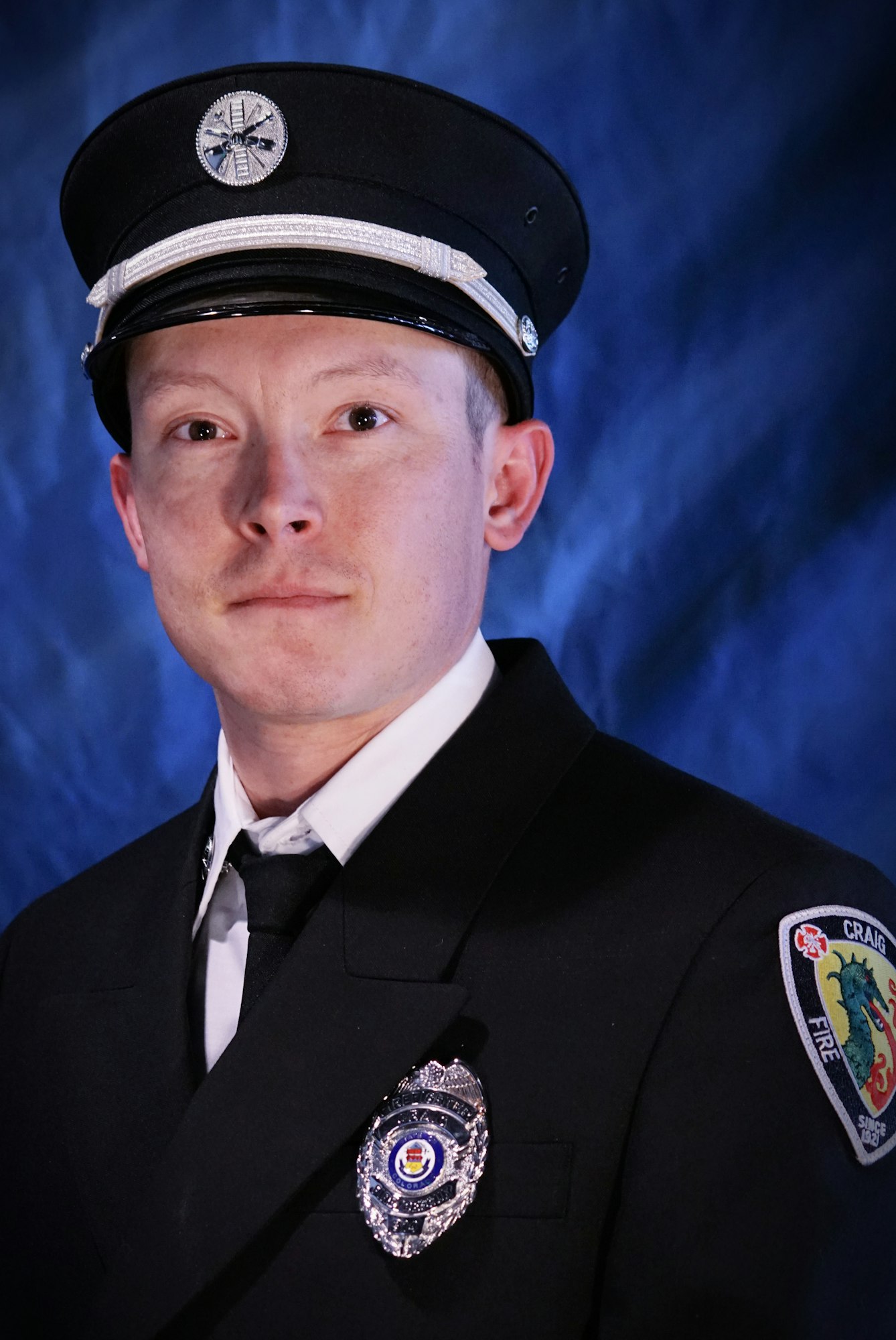 A person in a formal firefighter uniform with a badge and cap.