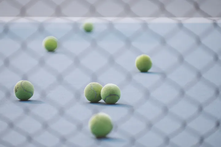 Tennis balls scattered on a court with a net in the background.