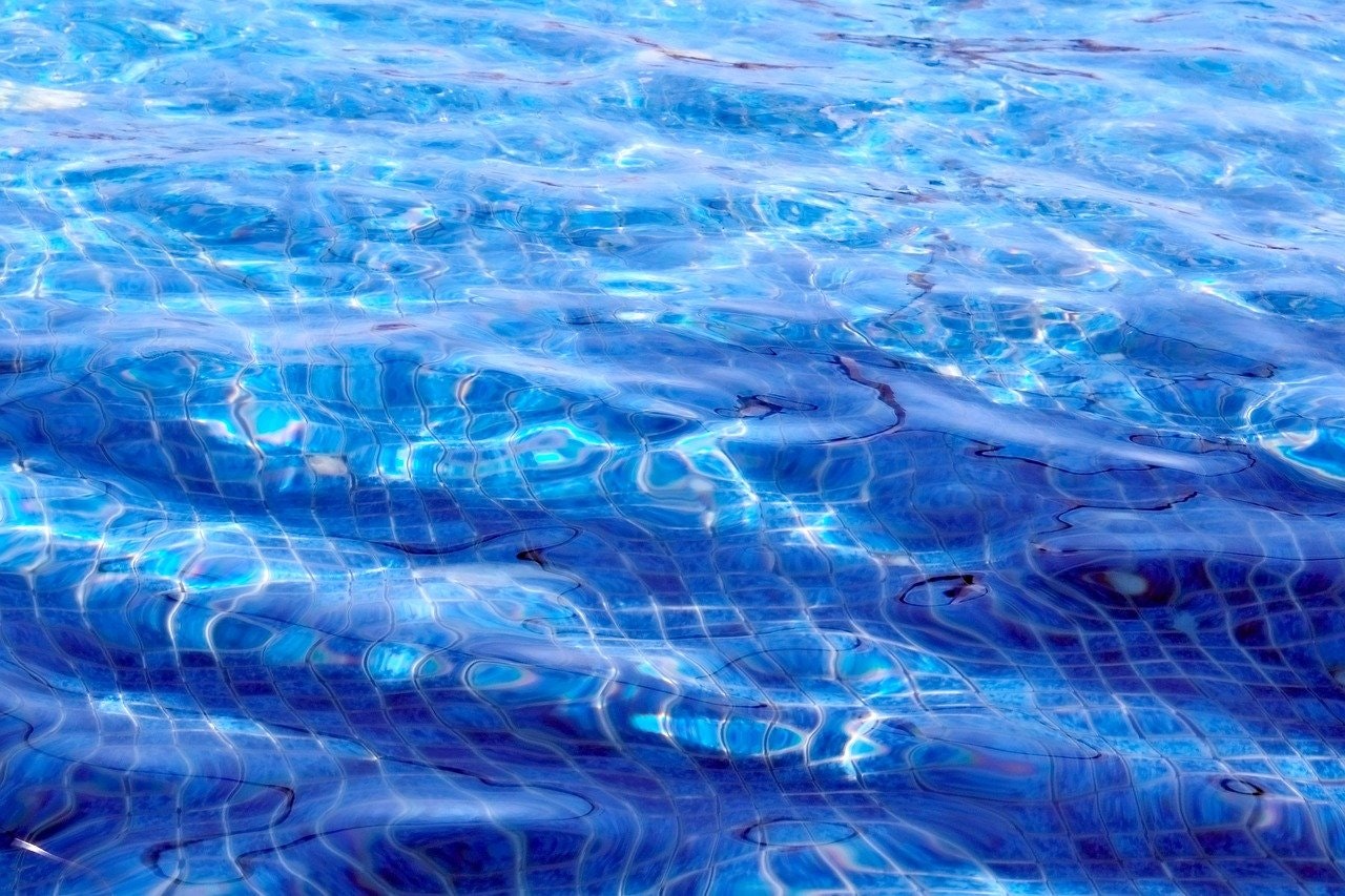 Sunlight dances on the rippling water of a swimming pool.