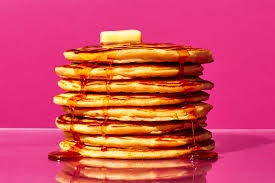 Stack of pancakes with syrup and butter, against a pink background.